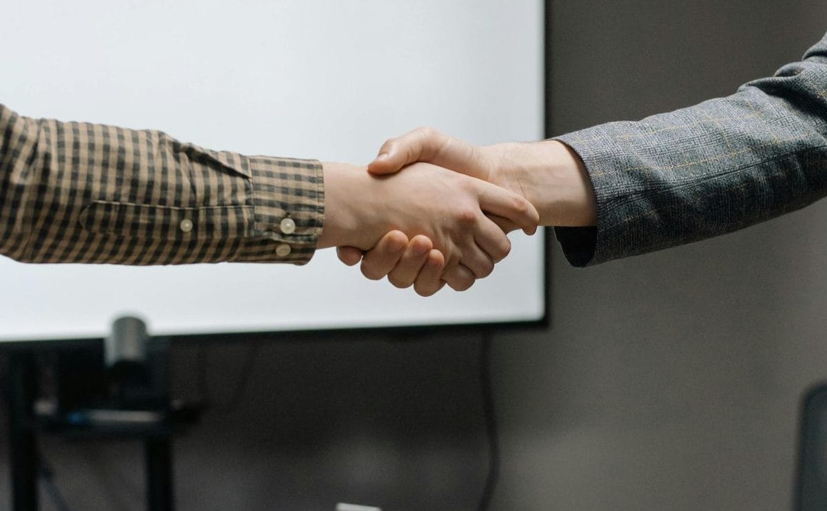Two business professionals shaking hands in a modern office, representing a legally binding agreement and the positive impact of a stable legal environment of business on global partnerships.